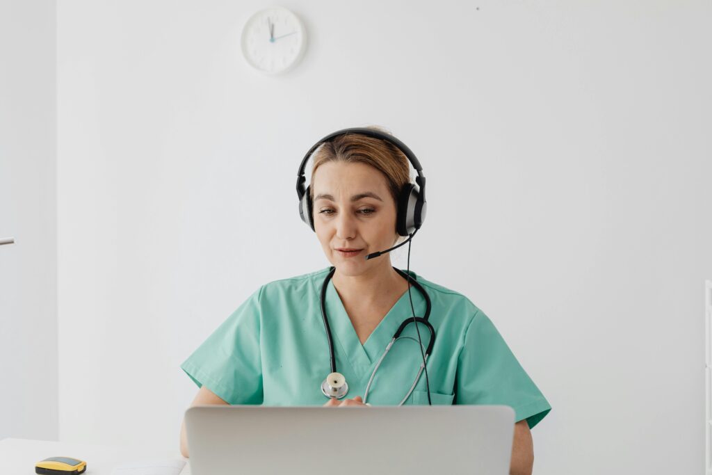 A female doctor in scrubs using a laptop for a virtual consultation, enhancing telemedicine.